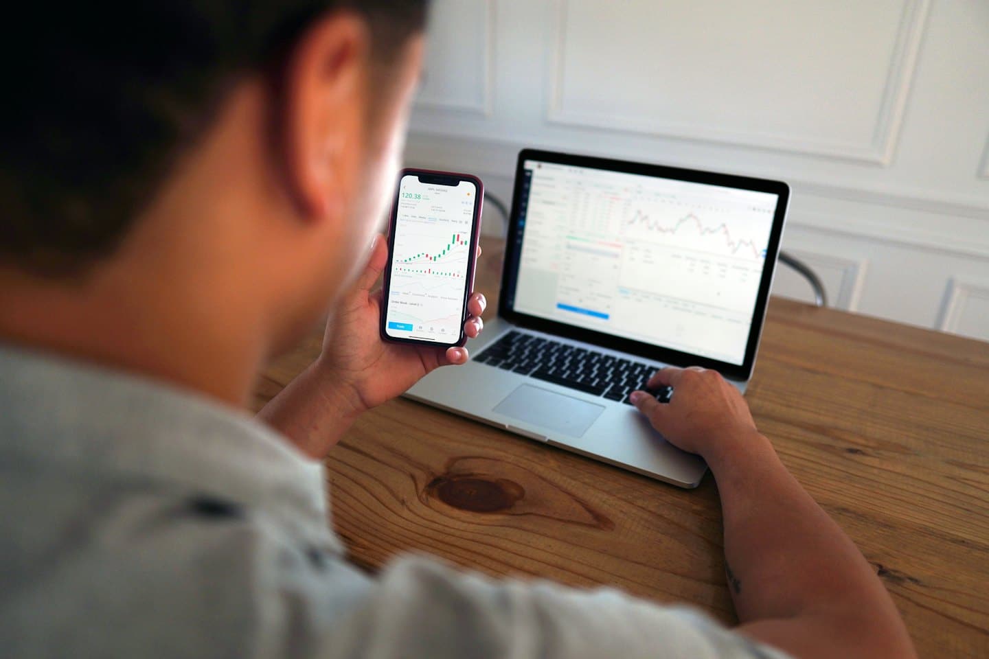 Person prüft Aktiencharts auf Handy und Laptop.