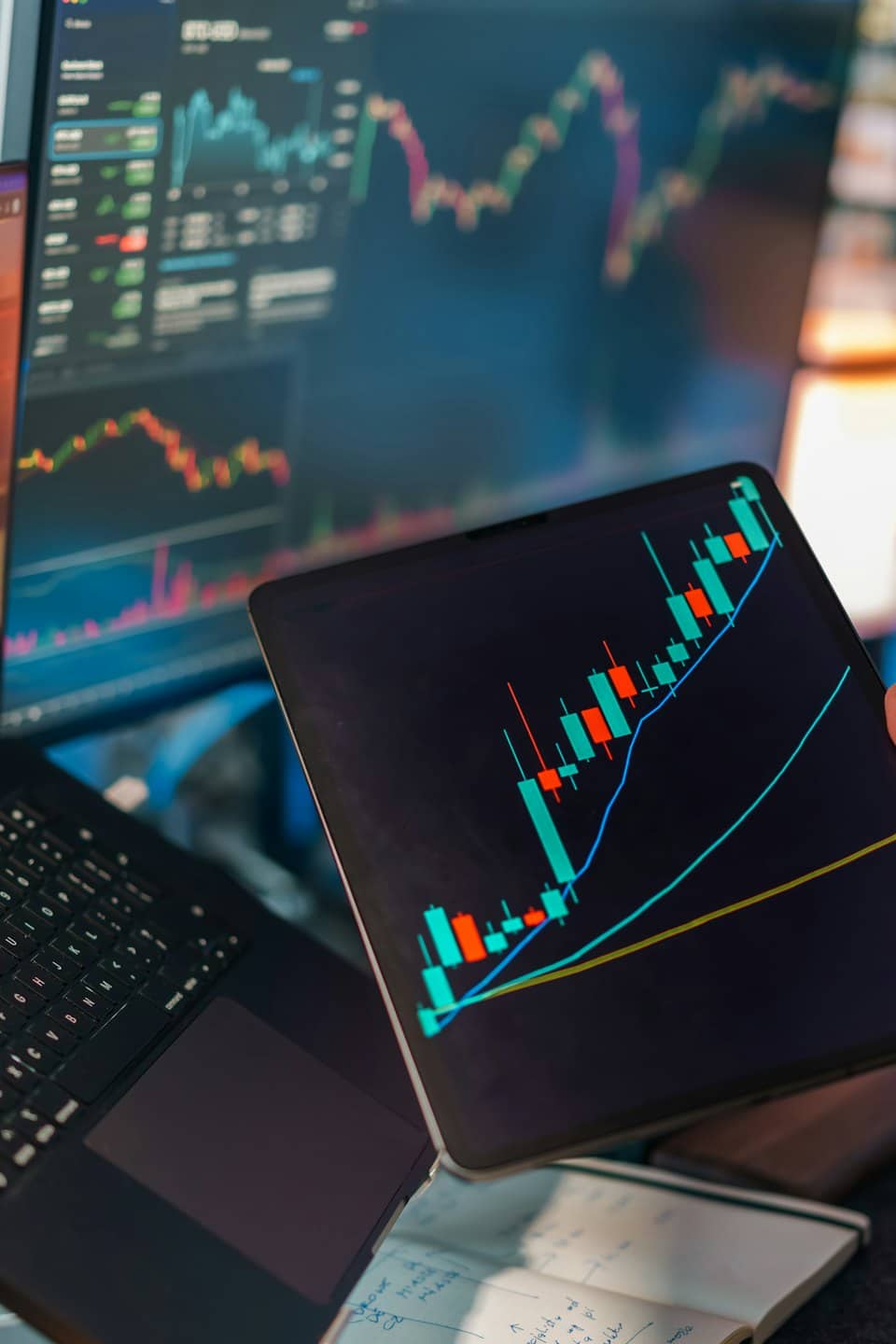 Hand hält ein Tablet mit Finanzdiagramm über einem Laptop.